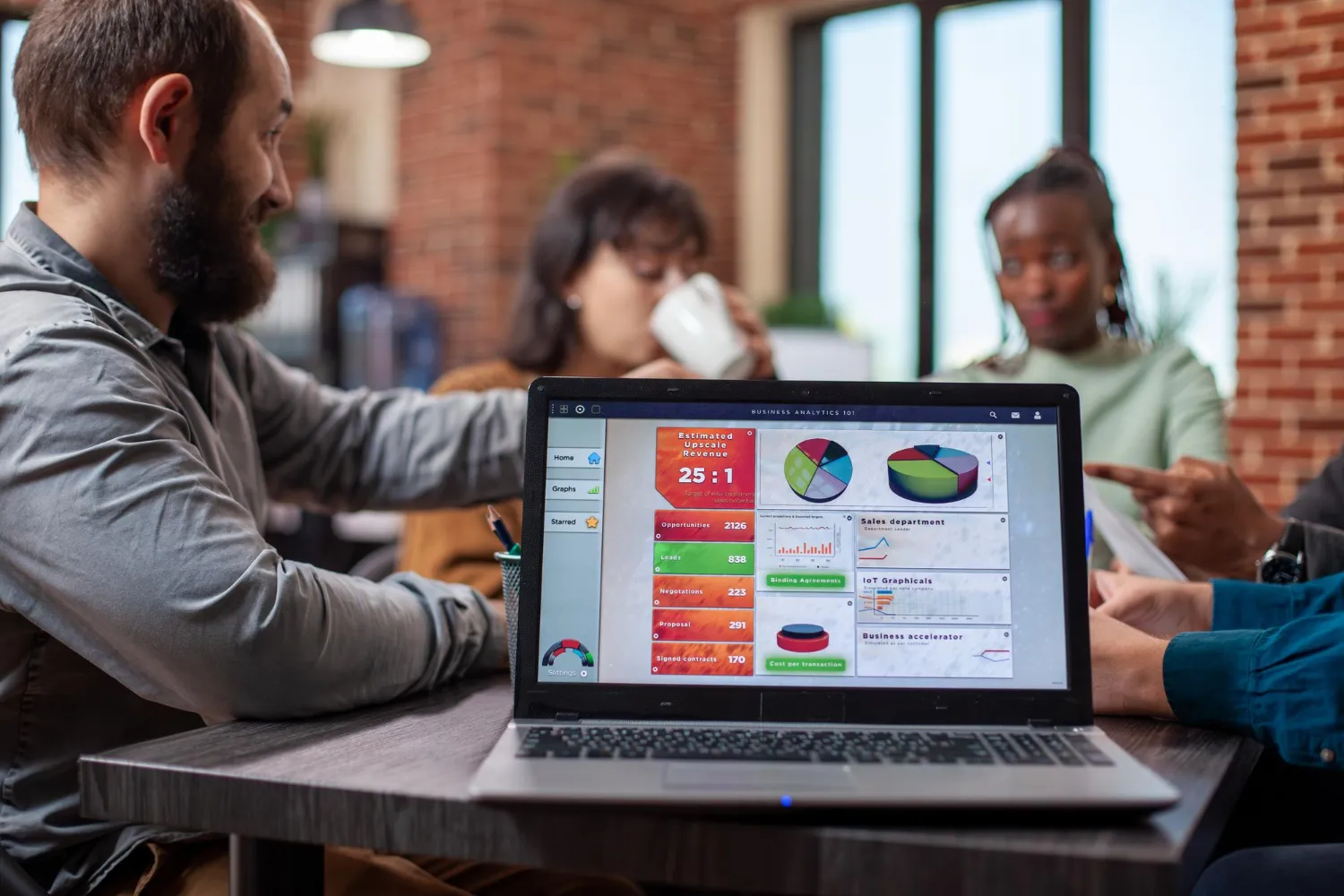 A group of coworkers in an office discussing business analytics while viewing charts and graphs on a laptop screen.